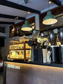 Modern coffee shop counter with glowing pastry case, hanging lights, and espresso machines