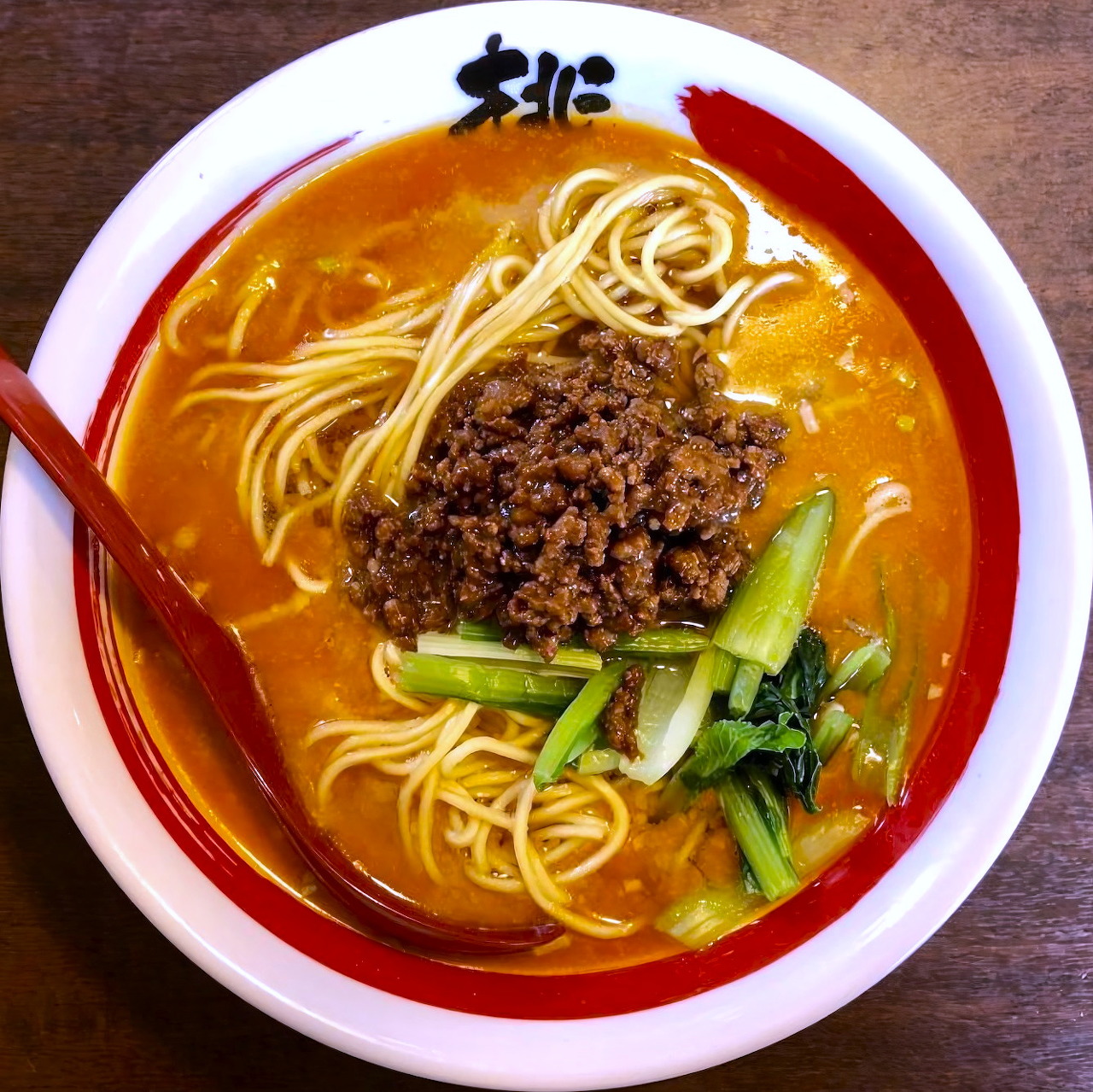 Bowl of tantanmen ramen with noodles, minced meat, bok choy, and spicy broth viewed from above
