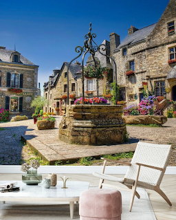 Stone well in sunny French village square surrounded by traditional old houses with flowers