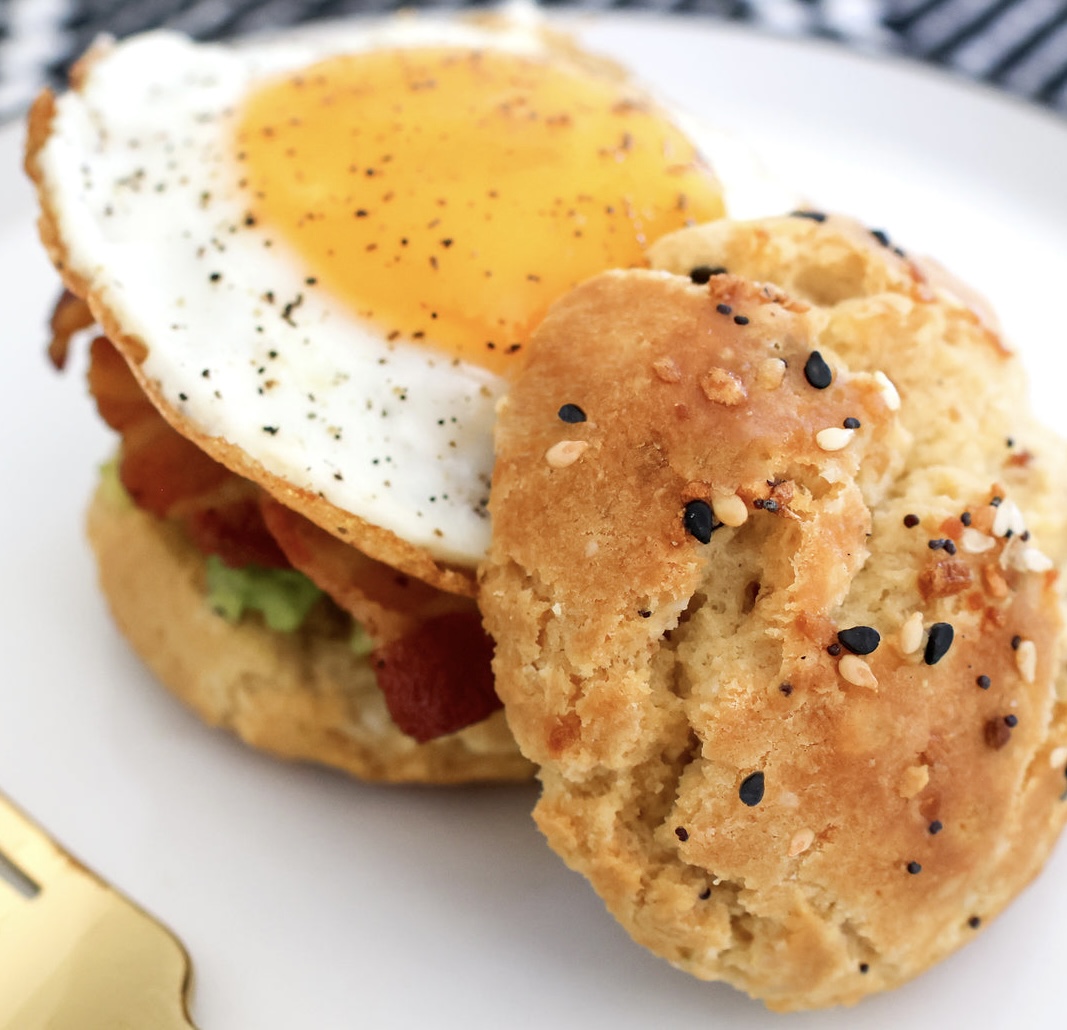 Breakfast sandwich with sunny-side-up egg on sesame bun with lettuce and tomato on white plate