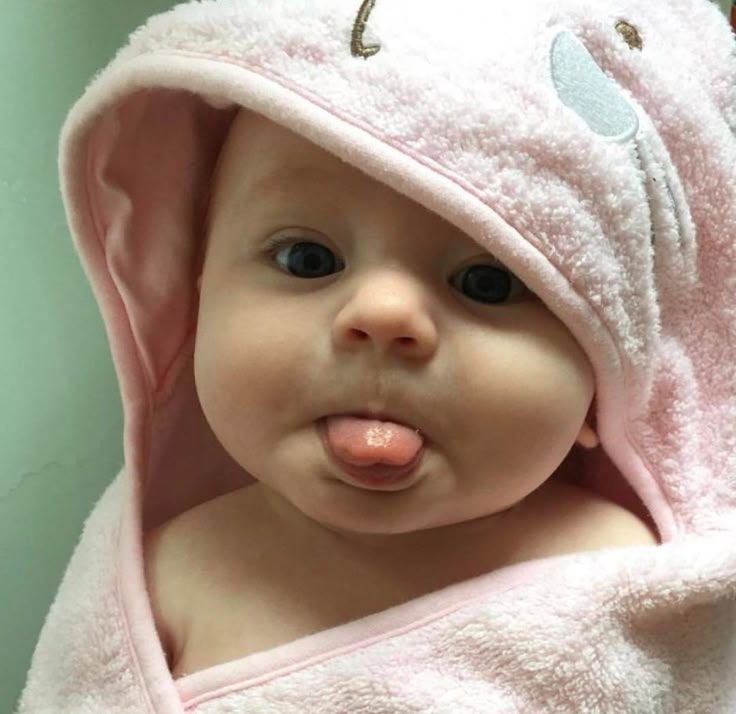 Baby in pink hooded towel with ears sticking tongue out