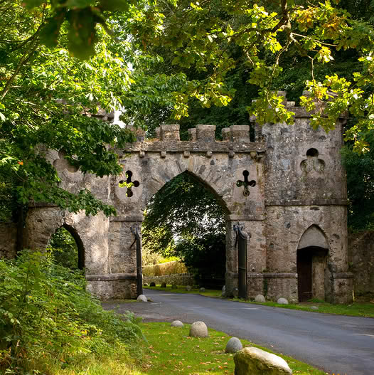 Old stone castle gate with arches beside a road under leafy trees