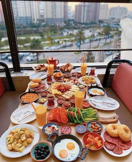 Colorful brunch table with assorted breakfast foods and beverages by a window overlooking a city