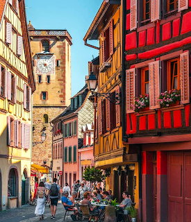 Colorful historic buildings on a narrow street in Ribeauvillé with outdoor cafés and a medieval tower