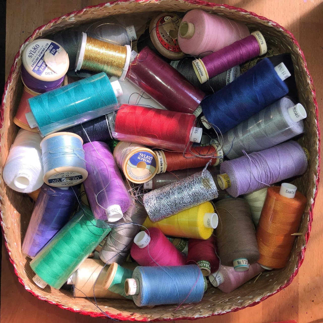 Wicker basket filled with colorful sewing thread spools in various colors on wooden surface