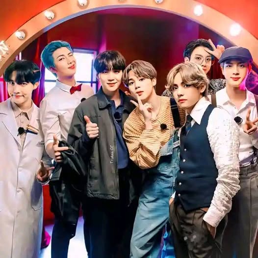Seven BTS members posing together in coordinated outfits under glowing lights