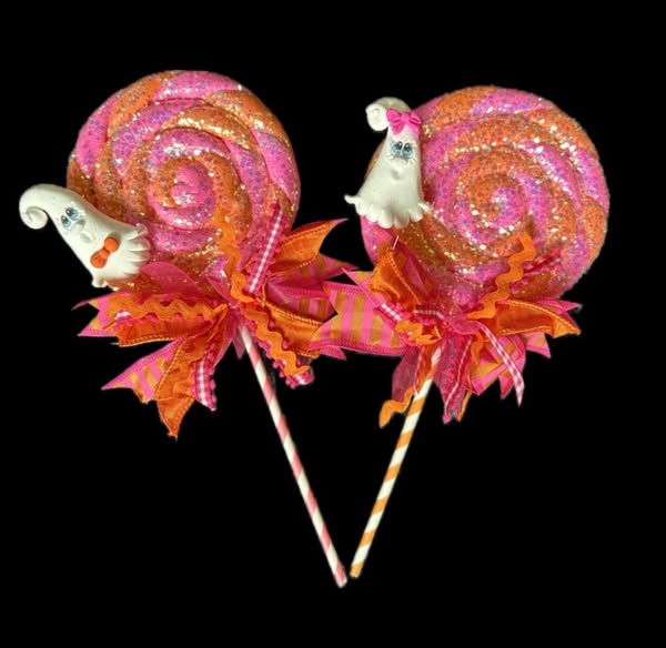 Two glittery orange spiral lollipops with white ghost decorations and orange ribbon bows