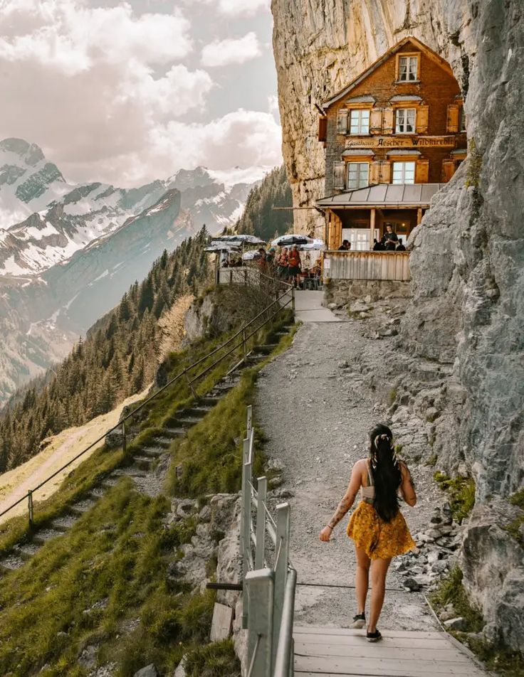 Woman walking on a cliffside path beside Aescher guesthouse in the Swiss Alps