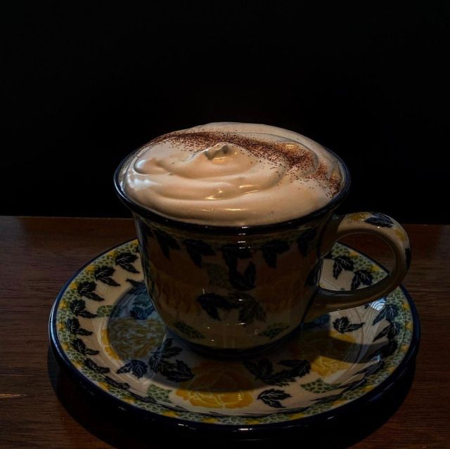 Cappuccino with foam in decorative cup and saucer on wooden table against black background