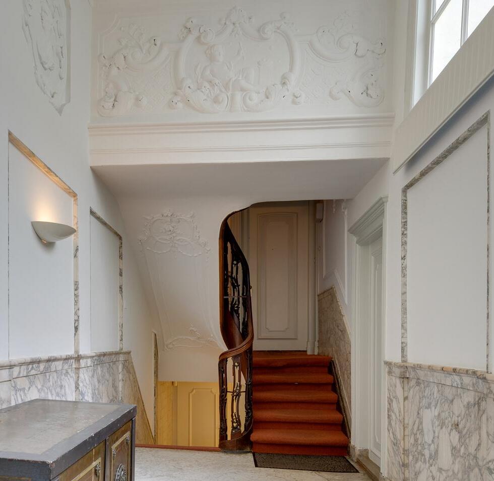 Historic Amsterdam house interior with decorative ceiling, marble walls, and wooden staircase