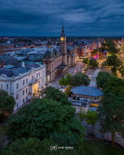 Aerial view of historic city with clock tower at dusk, lit streets and cloudy blue sky