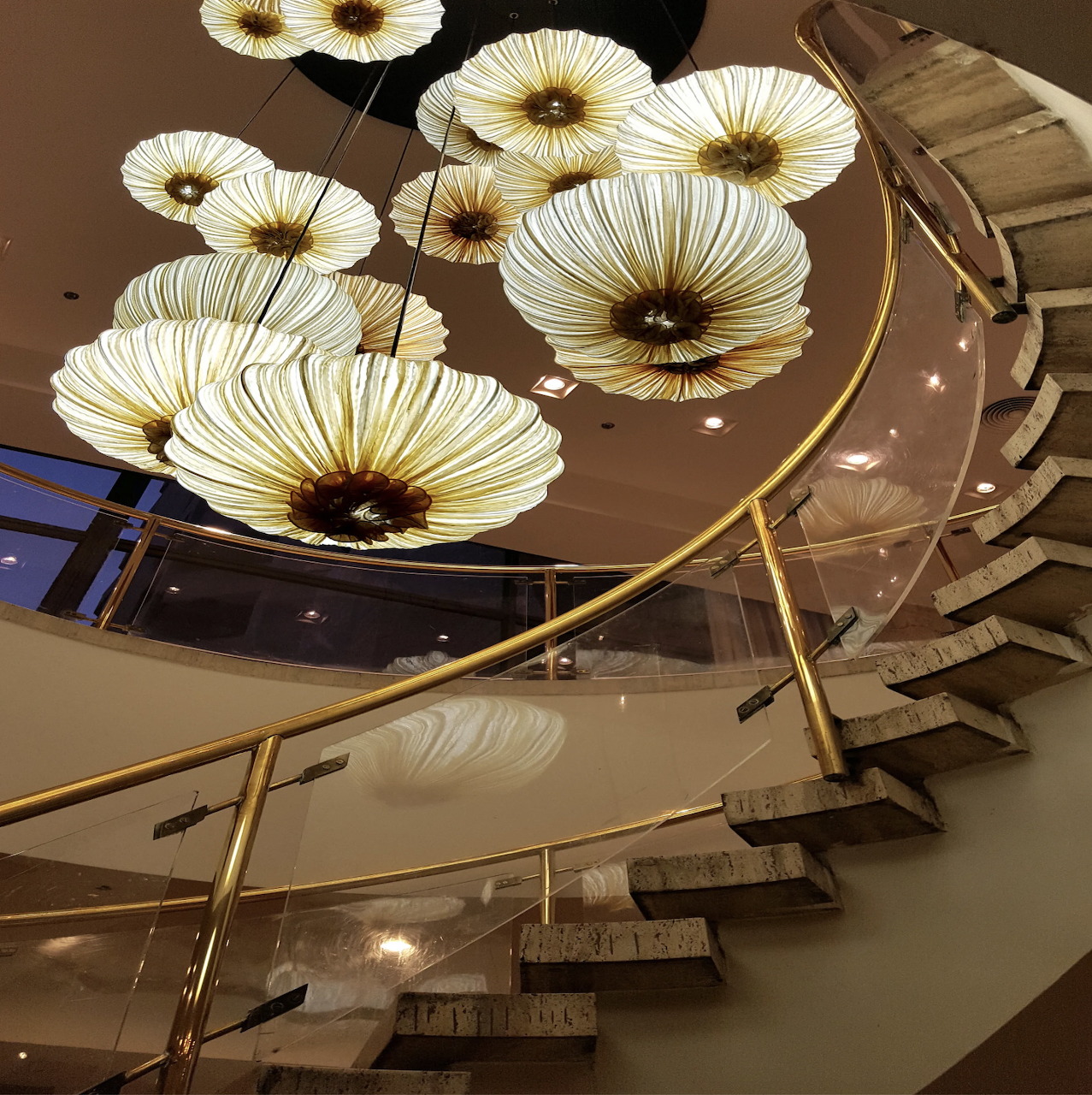 Curved staircase beneath large flower-shaped pendant lights in a hotel lobby