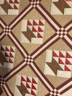 Geometric patchwork quilt with red, cream, and brown triangle blocks in a diamond pattern