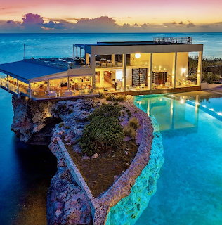 Modern luxury resort villa with infinity pool on rocky coast at sunset with ocean view