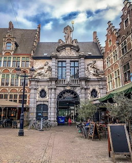 Ornate Baroque stone gate with statues in a Flemish city square surrounded by historic buildings