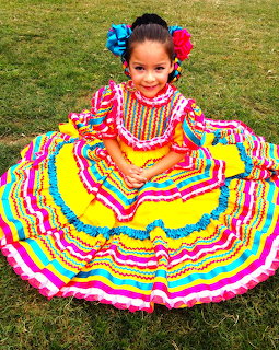 Girl in colorful traditional Mexican folkloric dress with ruffled layers sitting on grass