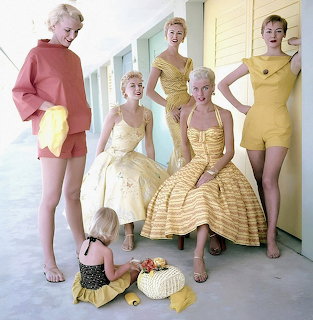 Five women in yellow 1950s summer fashion poses with child in bright hallway