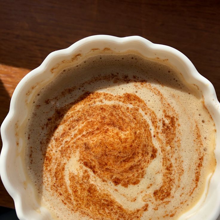 Overhead view of latte with cinnamon swirl in white scalloped cup on wood table
