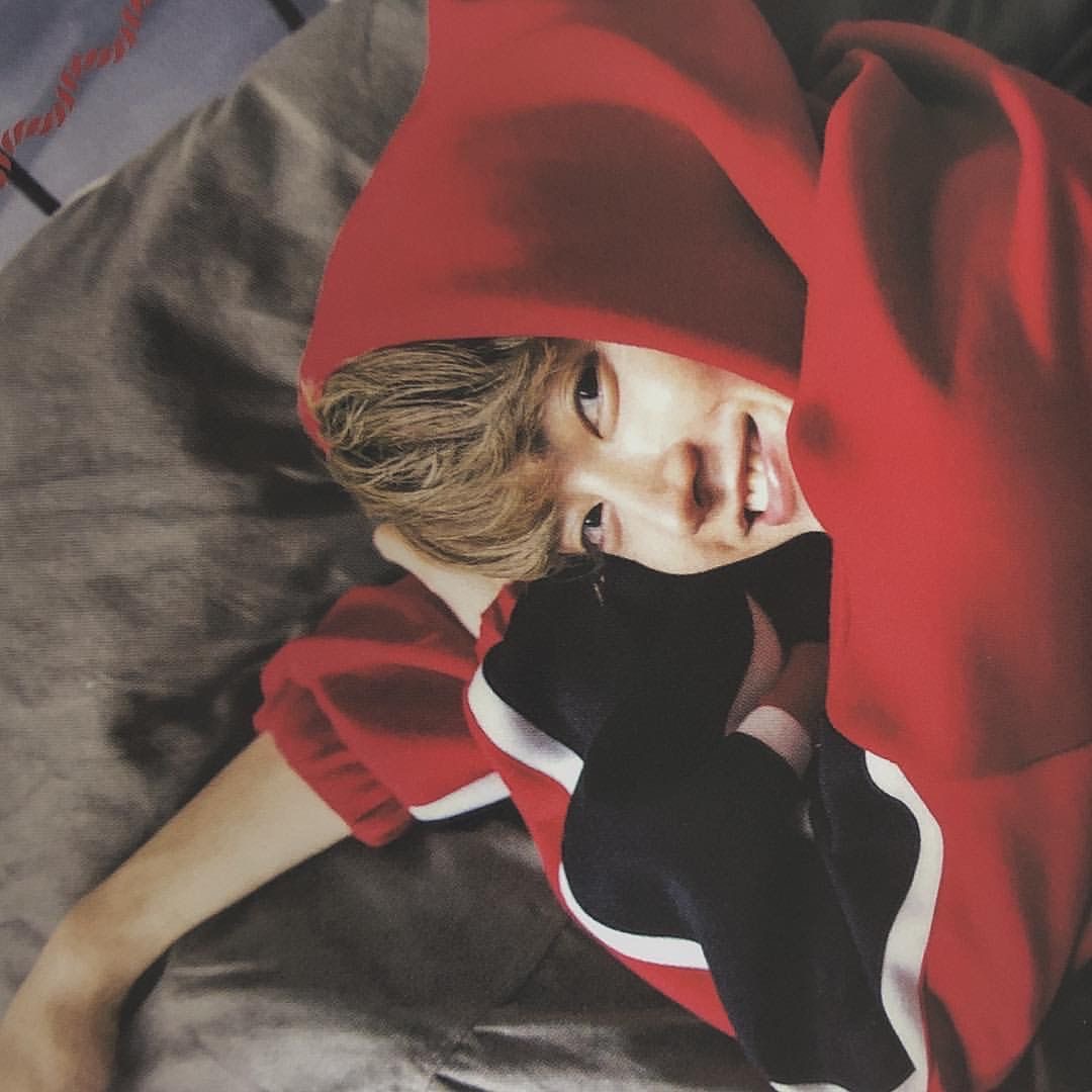 Person lying on a bed wrapped in a red blanket, looking at the camera