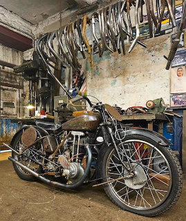 Vintage motorcycle parked in an old workshop with bicycle wheels hanging overhead