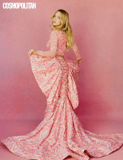 Blonde woman in long pink patterned dress looking over her shoulder against a pink backdrop