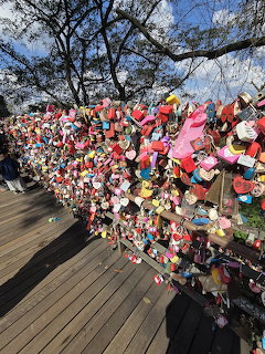 Colorful padlocks covering a fence beside a wooden walkway under leafless trees