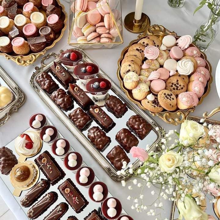 Overhead view of chocolate desserts, macarons, and cookies on elegant serving platters with white flowers