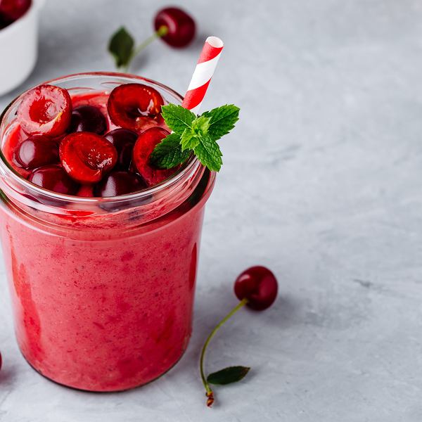 Red smoothie in jar with cherries and mint garnish on marble counter