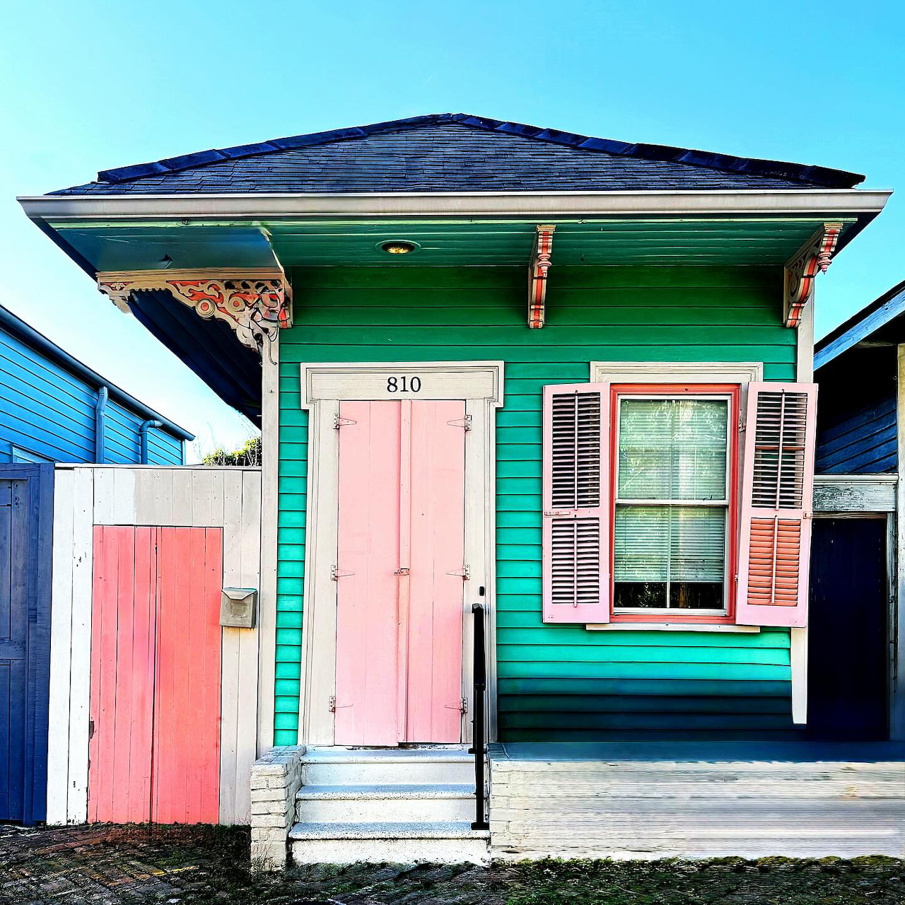 Small turquoise house with a pink door, pink shutters, and front steps