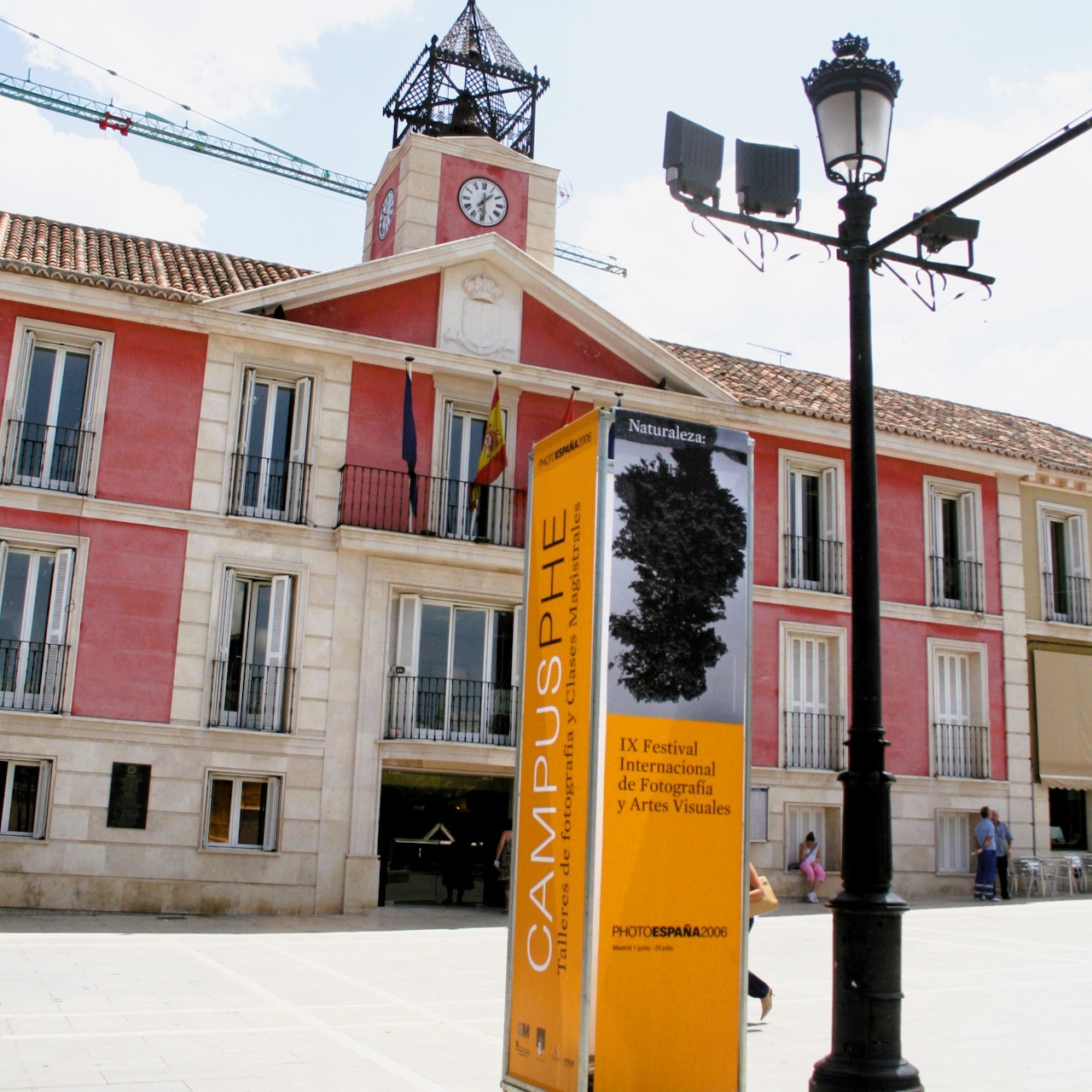 Pink building with a clock tower, streetlamp, and orange sign in a bright city square