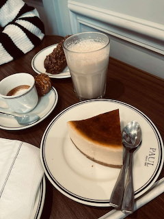 Cafe table with cheesecake slice on Paul plate, latte, espresso, and chocolate pastry