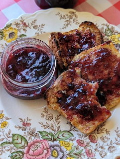 Glass jar of fruit jam next to jam-covered toast slices on a floral vintage plate