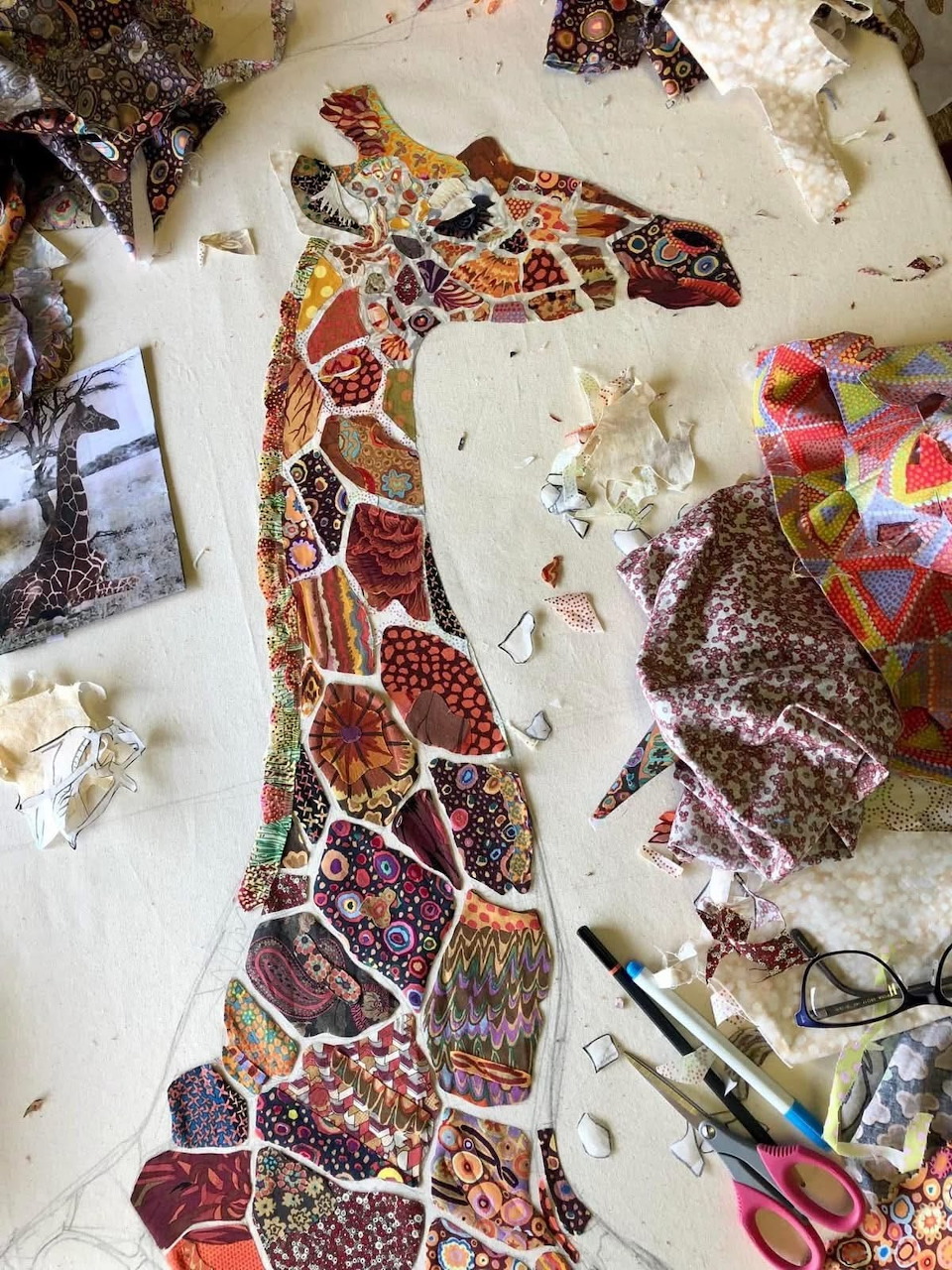 Colorful giraffe mosaic artwork on a messy craft table with paper scraps and scissors