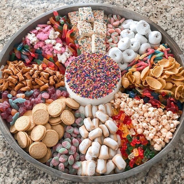 Round tray with colorful candy, sprinkles, cookies, mini donuts, popcorn, and assorted party snacks