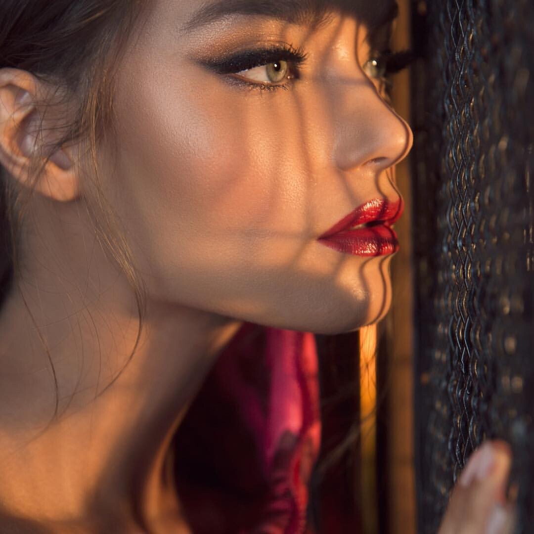 Close-up profile portrait of a woman with red lipstick and shadow patterns on her face