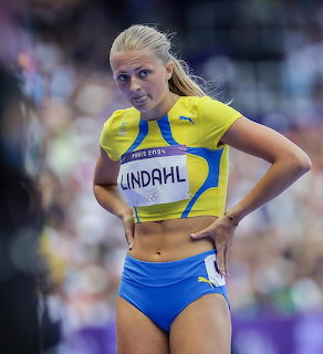 Female Swedish athlete in yellow crop top and blue shorts standing with hands on hips at athletics stadium