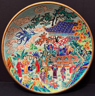 Colorful hand-painted decorative plate with figures, buildings, trees and detailed patterns on dark background