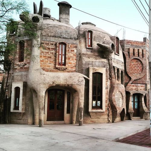 Unusual stone and brick house with animal-shaped columns and rounded organic design on a street corner