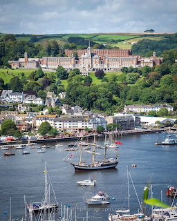 Dartmouth harbor with boats, waterfront buildings, and Britannia Royal Naval College on the green hillside