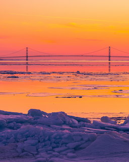 Vibrant orange and pink sunset over frozen icy landscape with distant bridge silhouette