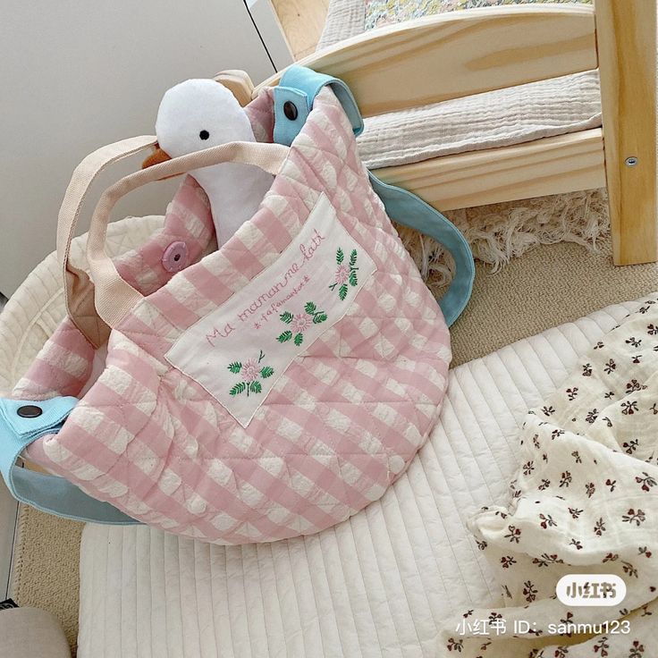 Pink gingham tote bag with plush toys on a cushioned chair beside a crib