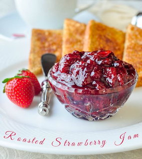 Glass bowl of dark red strawberry jam beside fresh strawberry and toasted bread slices