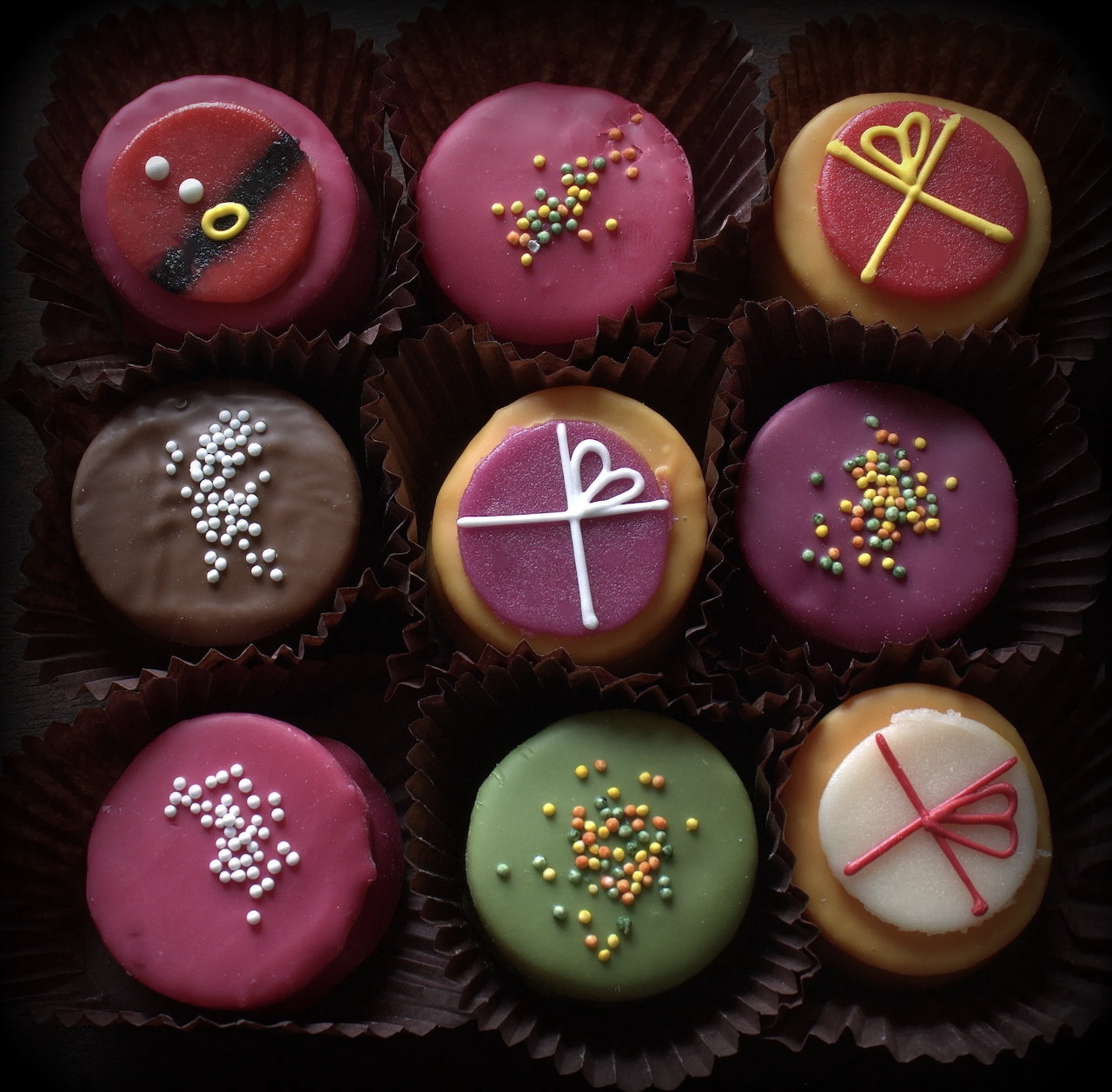Nine decorated chocolate truffles and sweets in paper cups on a dark background