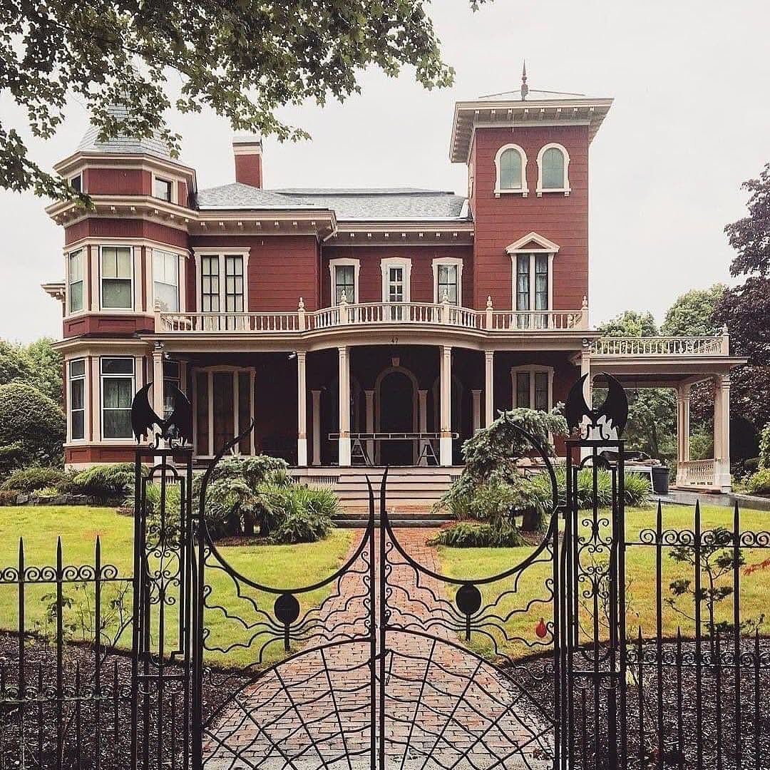 Red Victorian mansion with tower and porch behind ornate iron gate