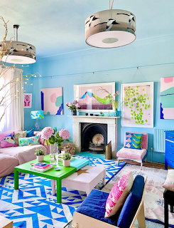 Colorful eclectic living room with blue walls, geometricrug, pink sofa, and framed artwork above fireplace