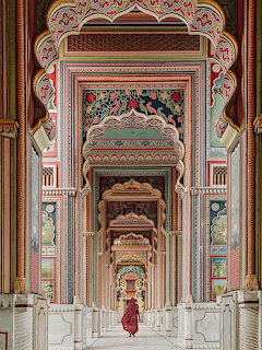 Ornate Indian palace corridor with decorated arches and woman in red walking through columned hallway