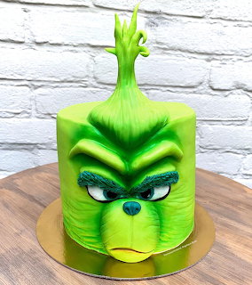 Green Grinch face cake on a gold cake board in front of a white brick wall