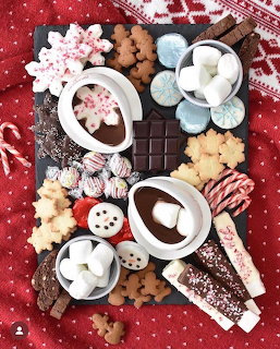 Holiday dessert board with hot chocolate, gingerbread cookies, marshmallows, candy canes, and chocolate on red fabric