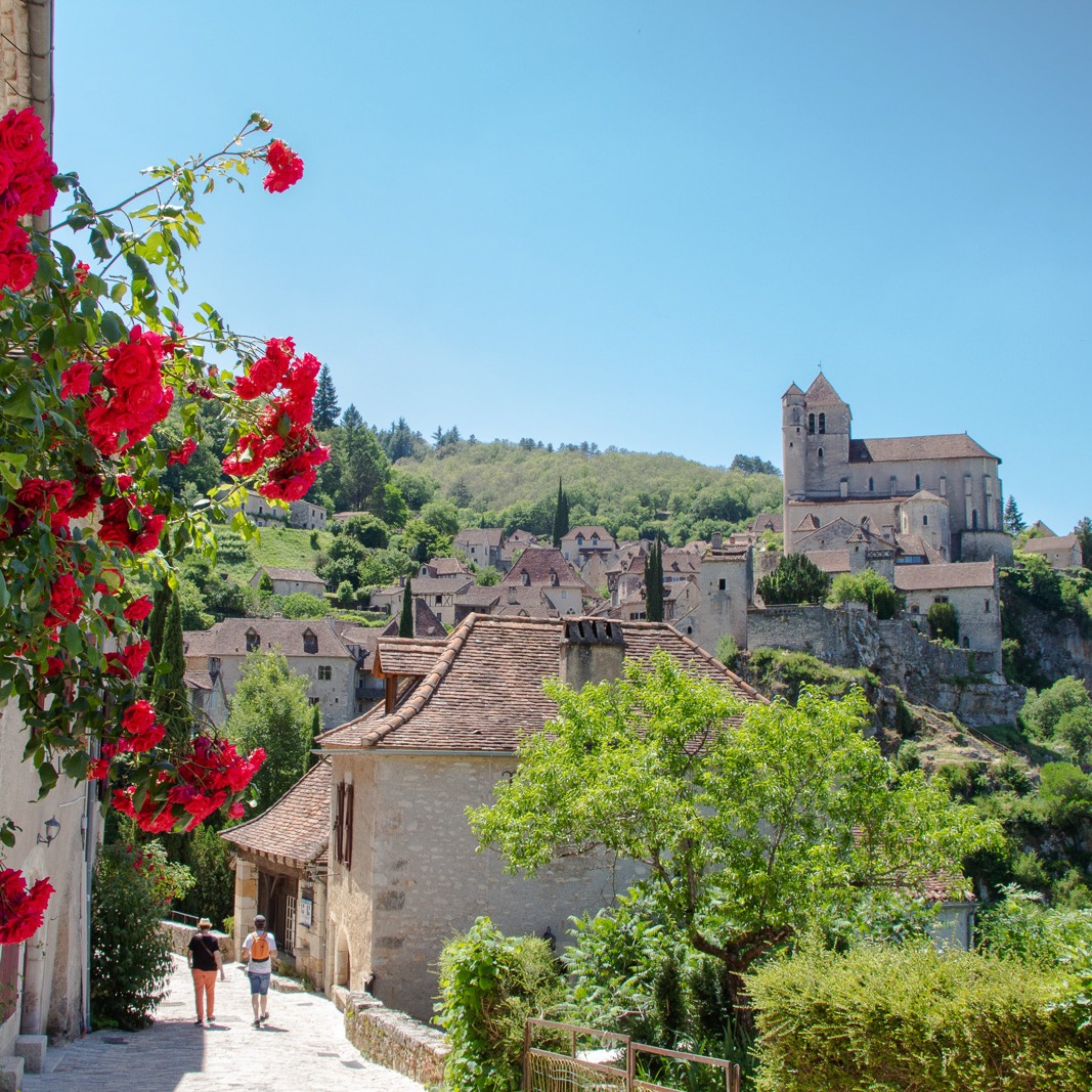 Medieval French village on hillside with church tower, stone houses, red climbing roses and green trees