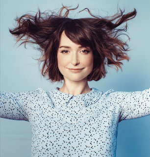 Woman with flowing brown hair in white polka dot sweater on blue background
